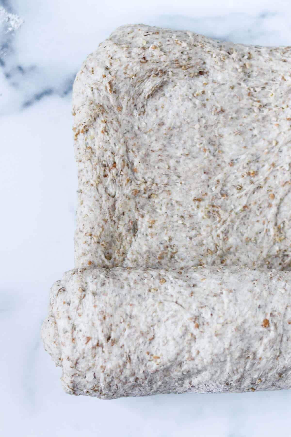 Rectangle of bread dough being rolled up on a marble surface.