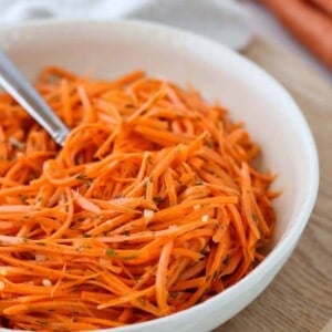 Raw Carrot Salad with Dill and Lemon in a bowl next to two carrots.