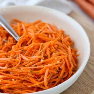 Raw Carrot Salad with Dill and Lemon in a bowl next to two carrots.