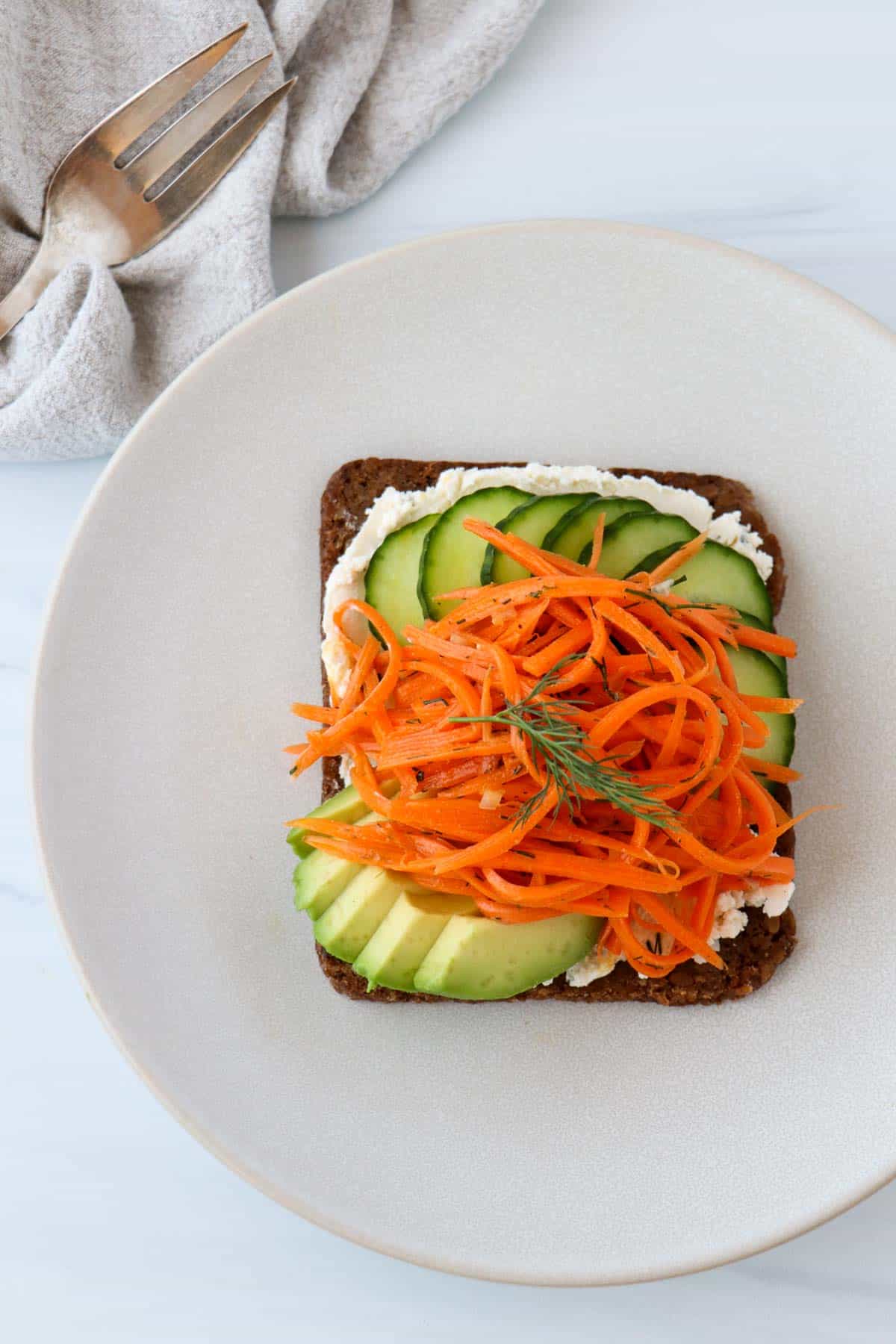 Carrot Salad Smørrebrød on a plate next to a fork and napkin.