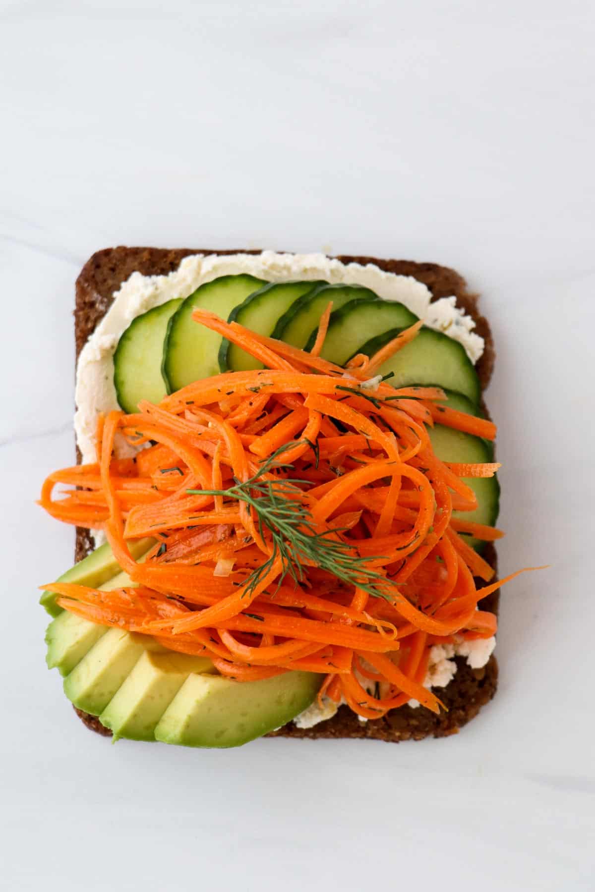 Overhead view of Carrot Salad Smørrebrød with Boursin, Cucumber and Avocado.