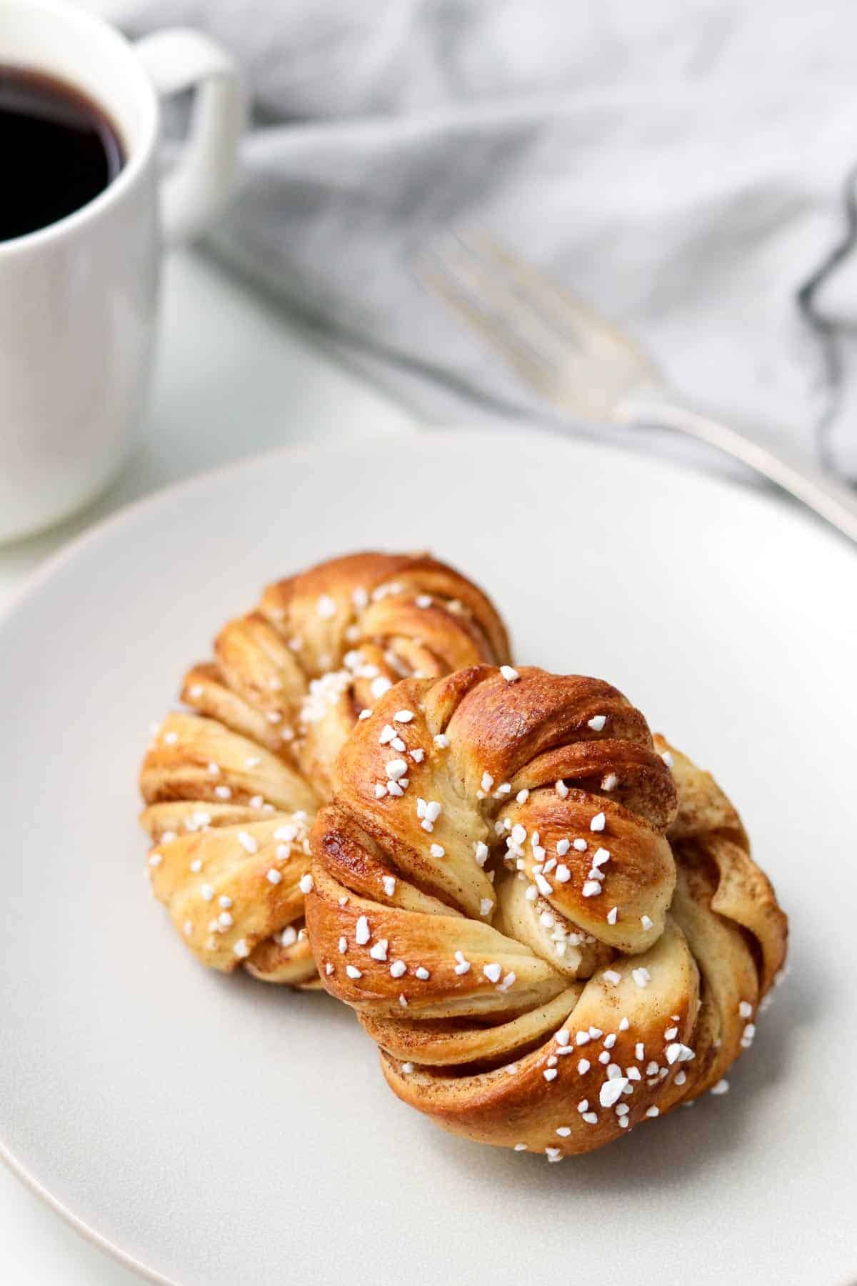 Swedish Cinnamon Buns on a plate next to a cup of coffee.