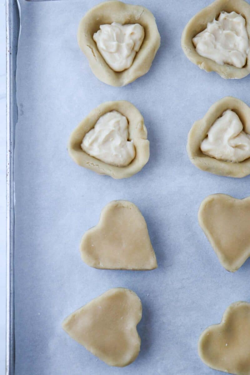 Pastry hearts on a baking sheet filled with pastry cream.