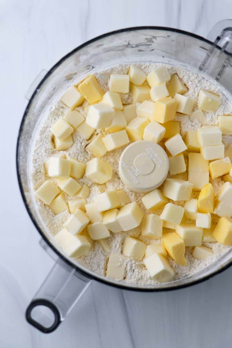 Flour and cubes of butter in the work bowl of a food processor.