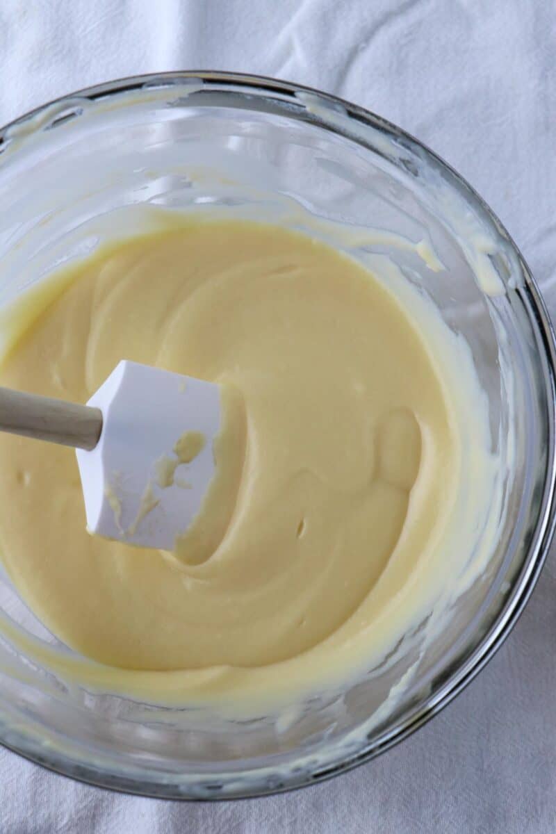Pastry cream in a glass bowl with a rubber spatula.