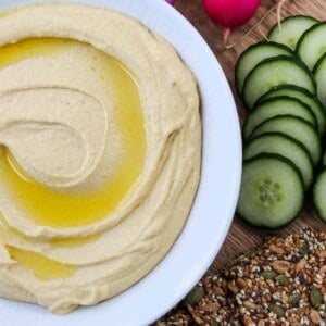 Split Pea Hummus drizzled with olive oil next to crackers, cucumber and radishes.