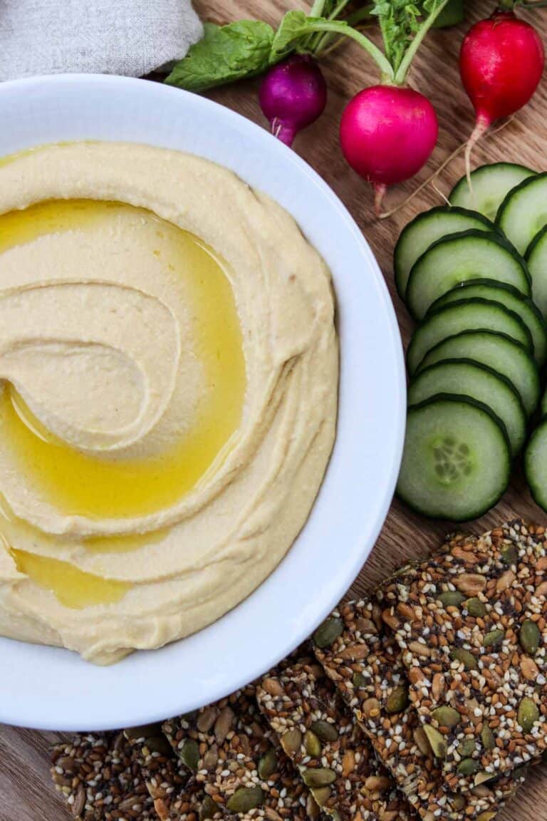Split Pea Hummus drizzled with olive oil next to crackers, cucumber and radishes.