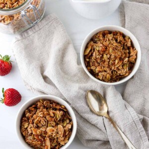 Overhead view of two bowls of granola, milk, berries and a spoon.
