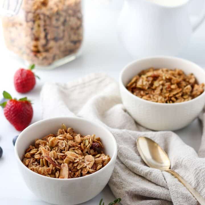 Granola in two bowls next to berries, milk and a spoon.