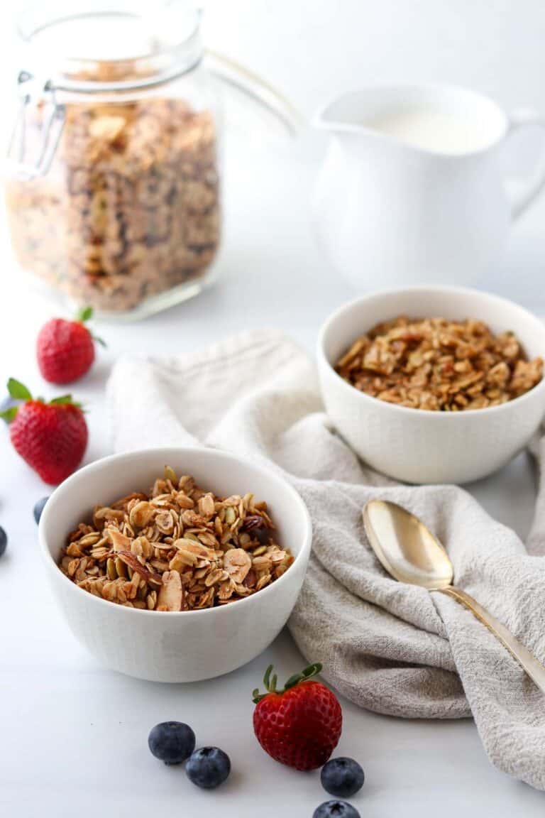 Granola in two bowls next to berries, milk and a spoon.