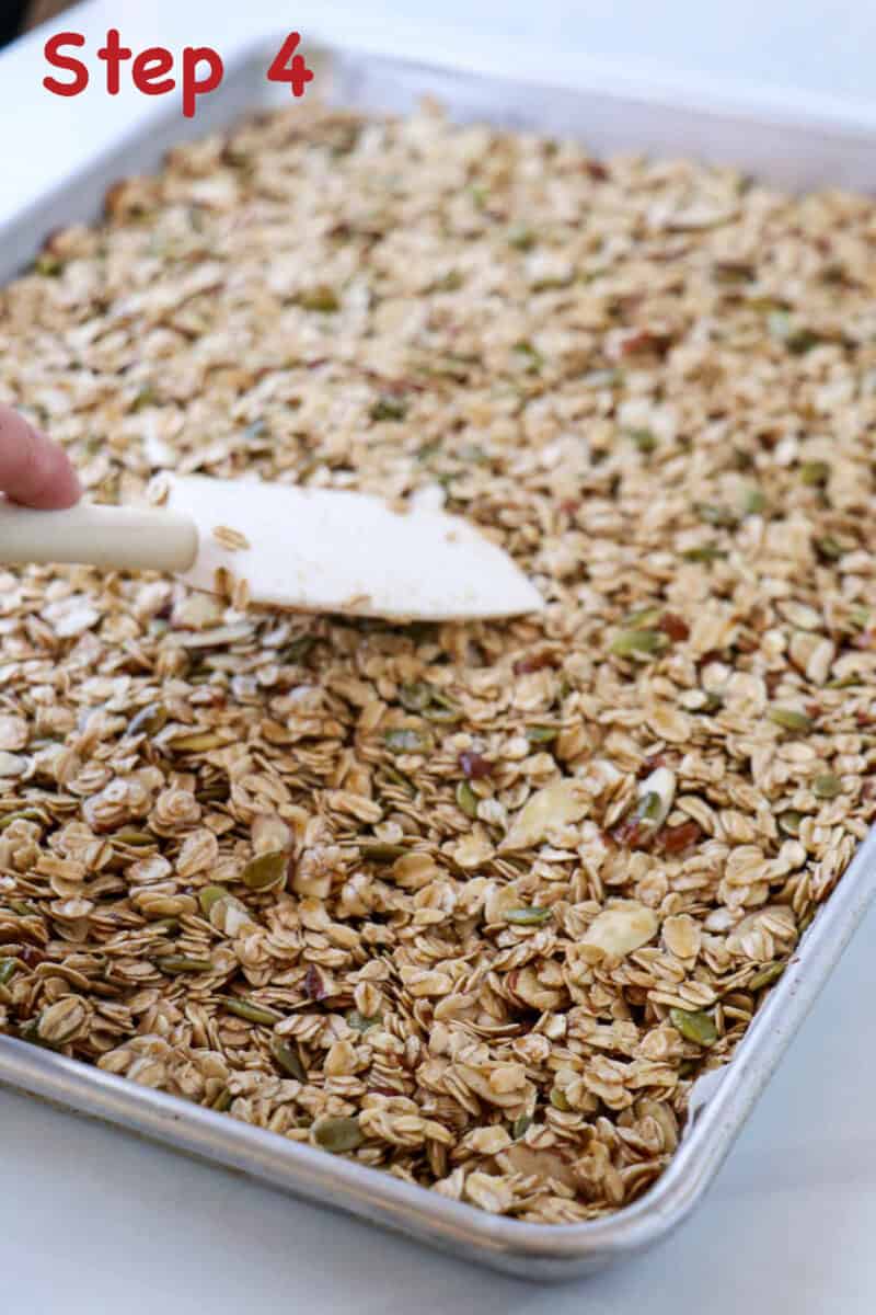 Unbaked Homemade Cardamom Granola with Almonds in a sheet pan with a rubber spatula.