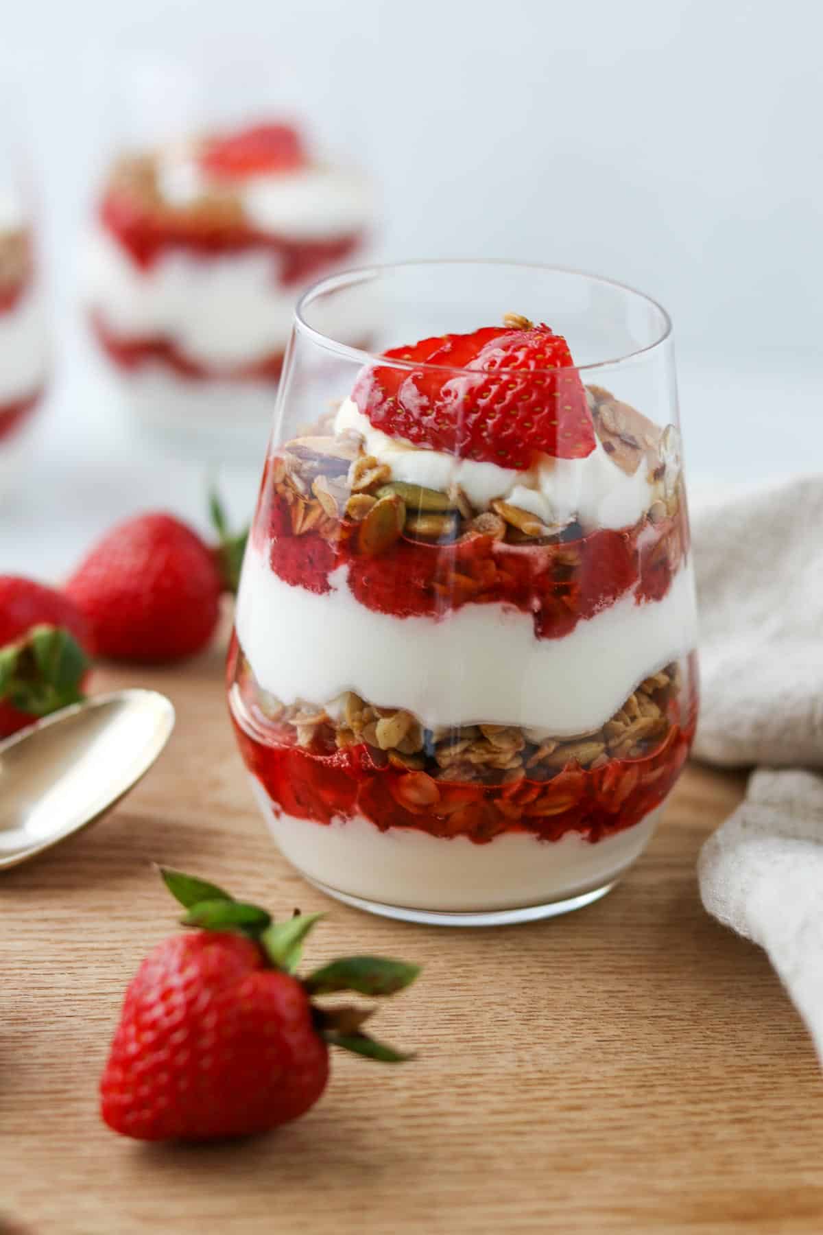 Yogurt, granola and strawberry parfait in a glass next to fresh strawberries.