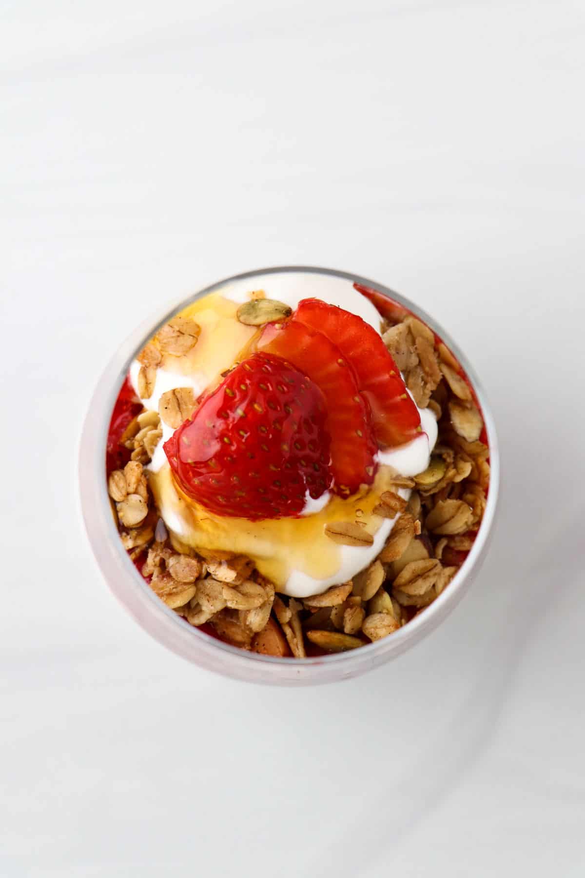Overhead view of granola, yogurt, strawberries and honey in a glass.
