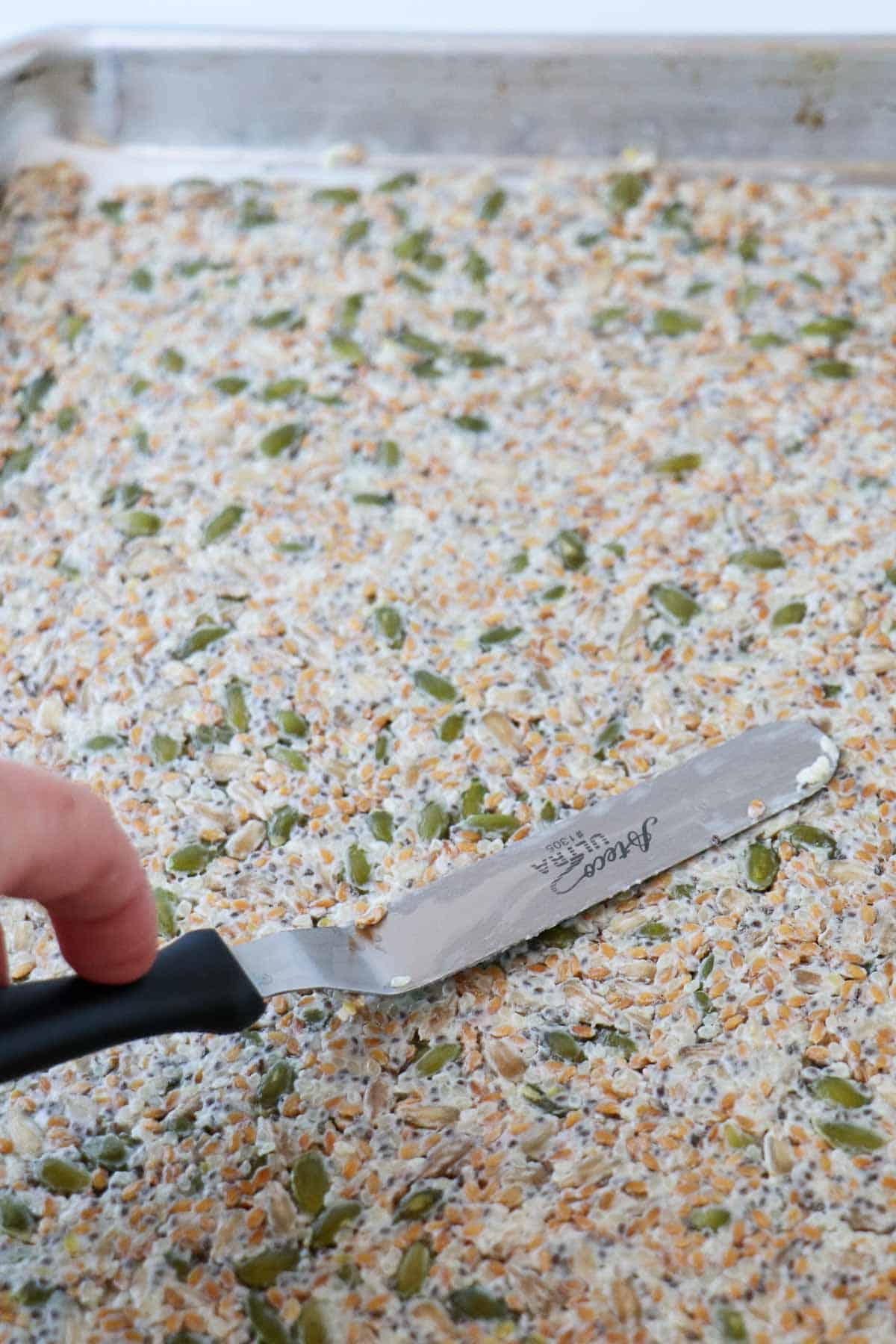 Person smoothing Norwegian Seed Crispbread on a baking sheet.
