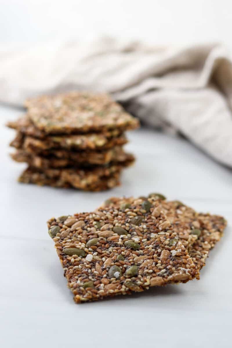 Pieces of Norwegian Seed Crispbread on a white surface with a kitchen towel.