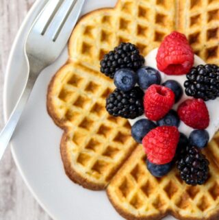Heart shaped waffle on a plate topped with whipped cream and fruit.