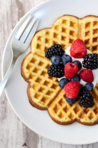 Heart shaped waffle on a plate topped with whipped cream and fruit.