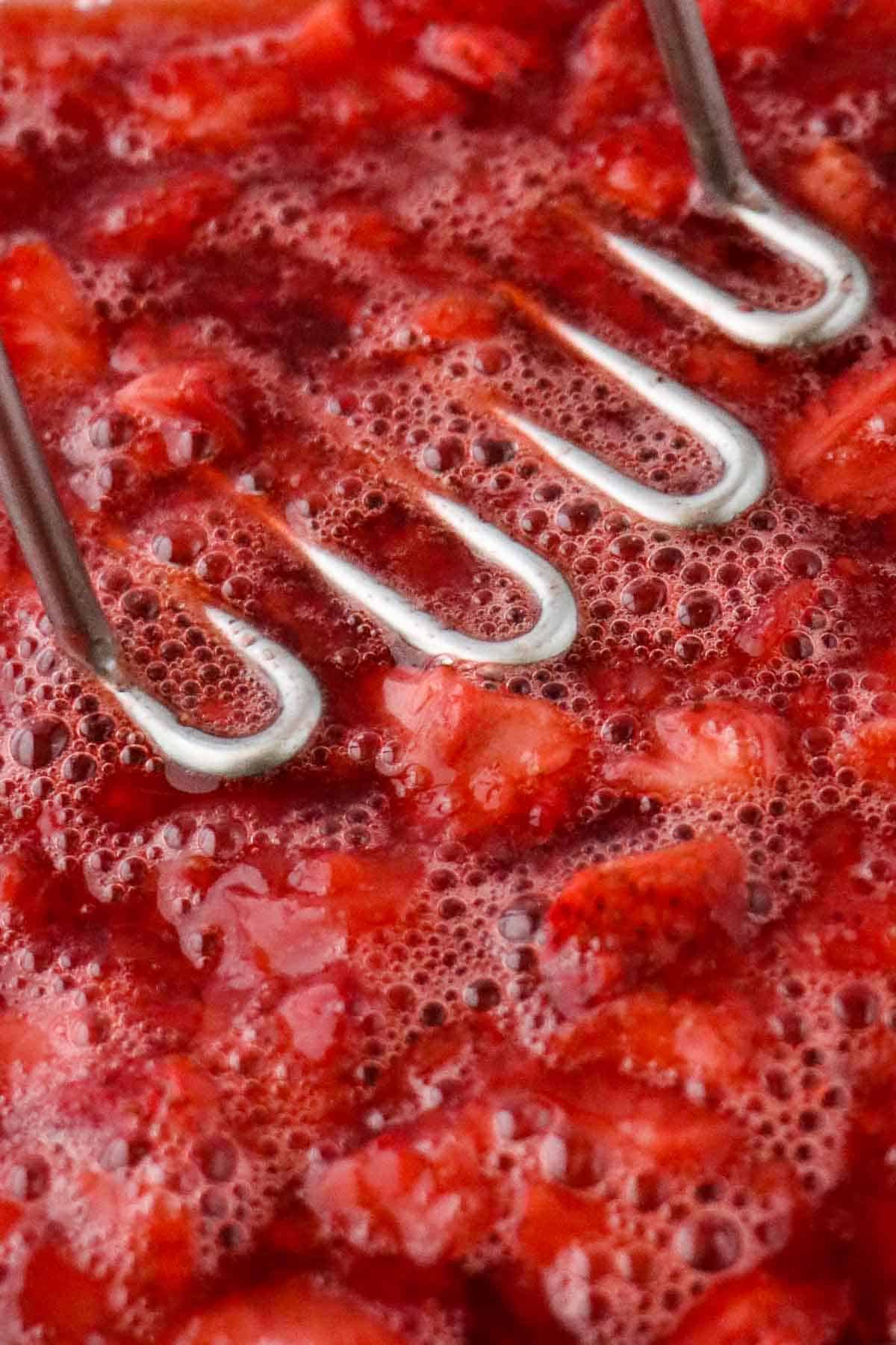 Roasted strawberries being mashed with a potato masher.