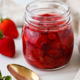 Jar of Roasted Strawberries next to fresh strawberries and a spoon.