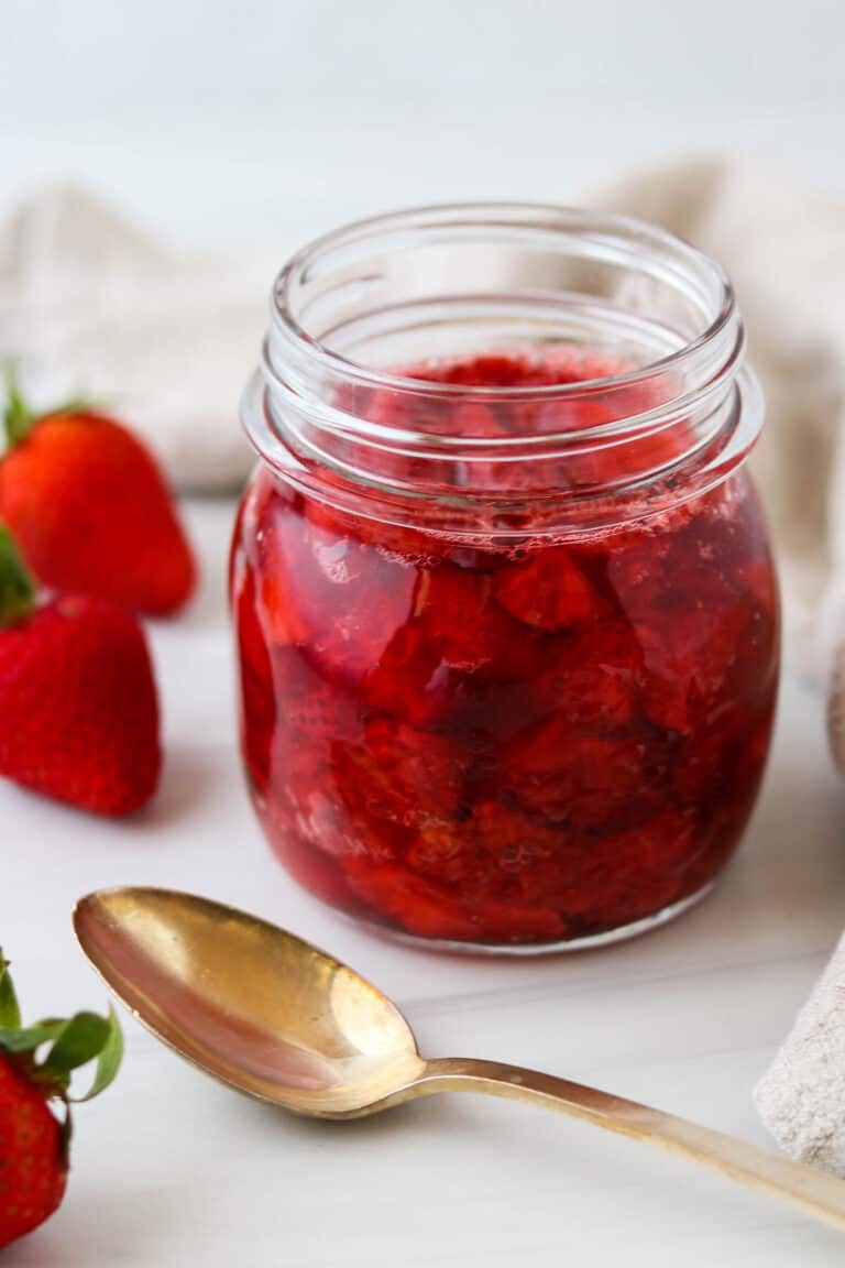 Jar of Roasted Strawberries next to fresh strawberries and a spoon.
