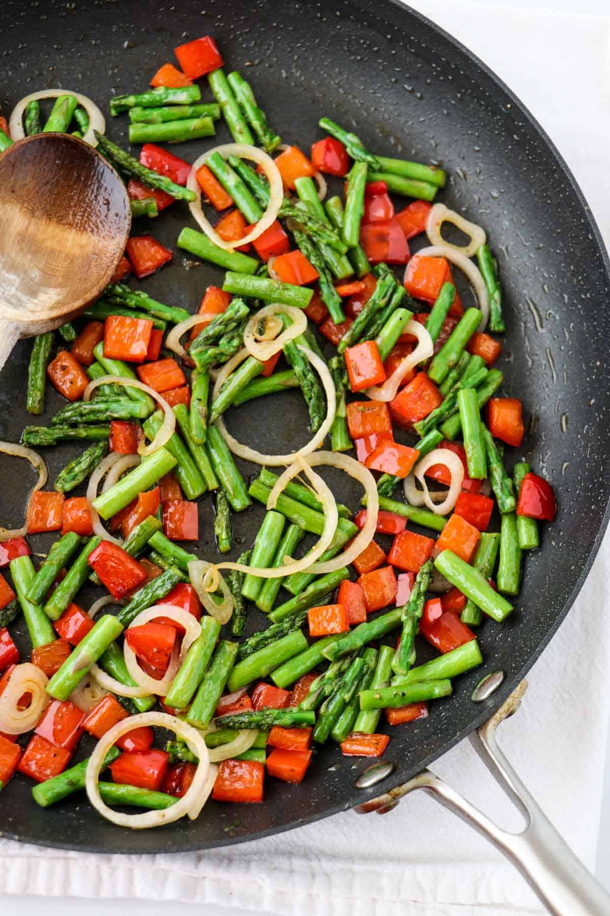 Red pepper, asparagus and shallot in a skillet with a wooden spoon.
