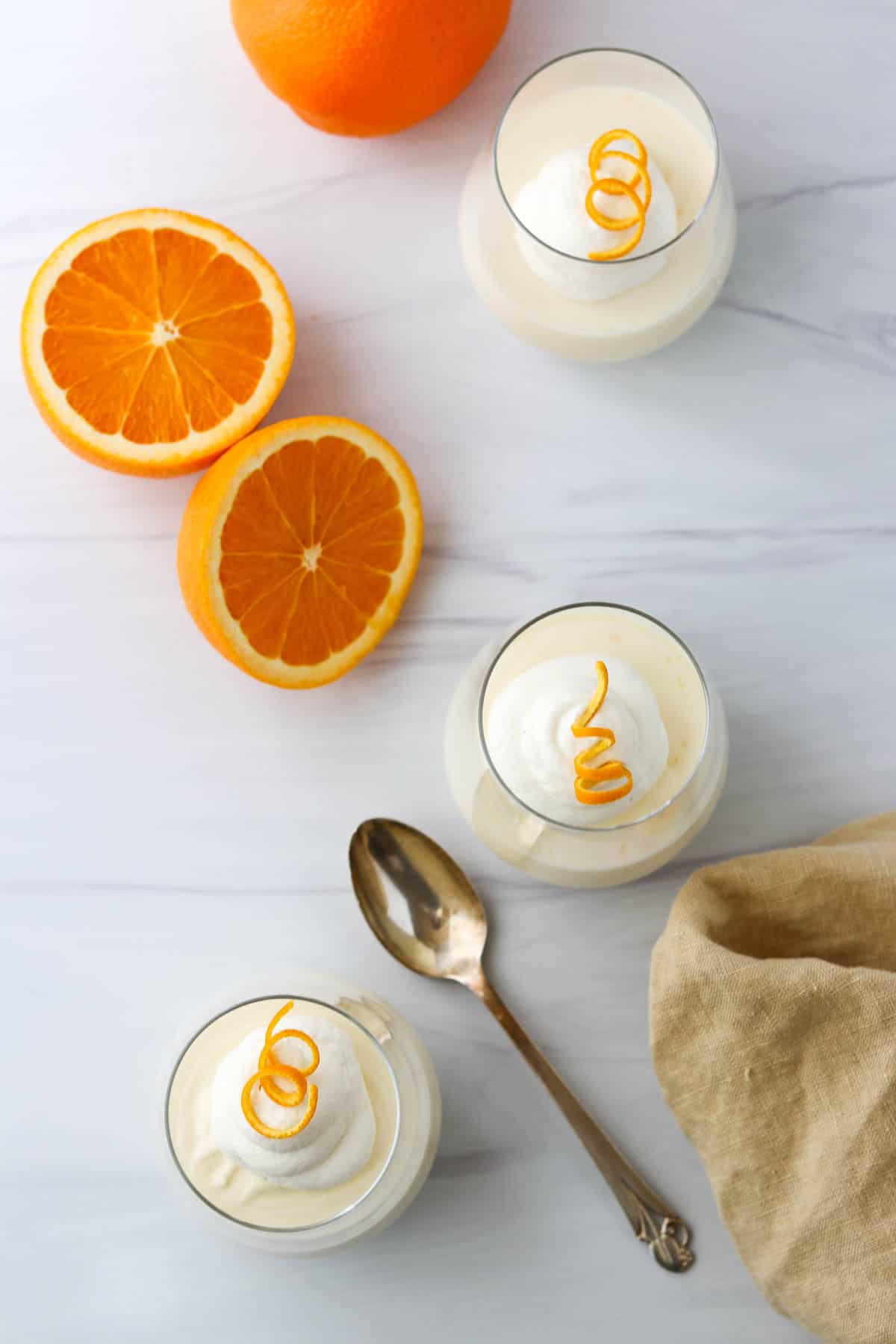 Overhead view of orange mousse and oranges next to a spoon and napkin.
