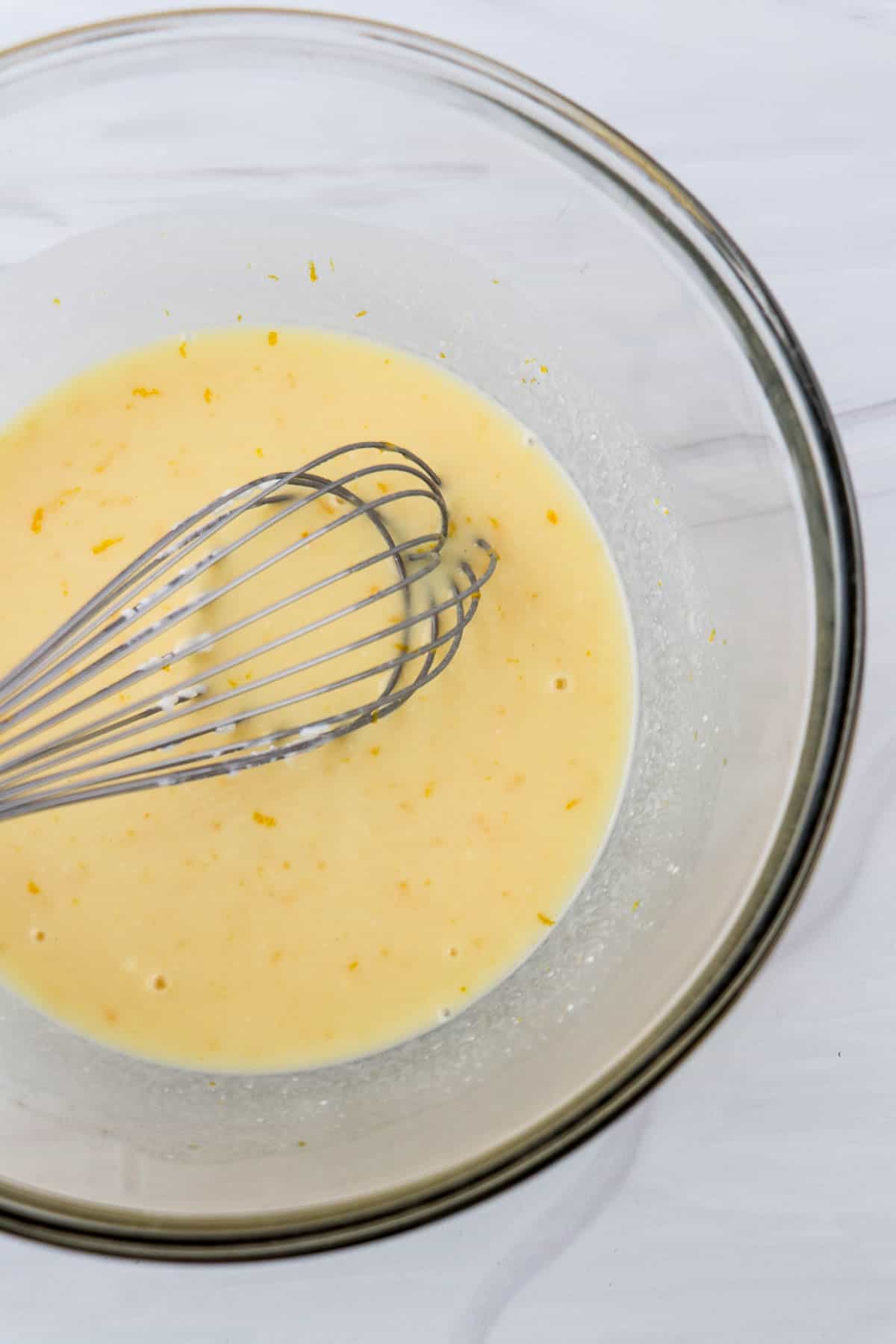 Orange juice and yogurt in a glass bowl with a whisk.