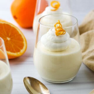 Light and Creamy Orange Mousse in a a glass next to a spoon and an orange.