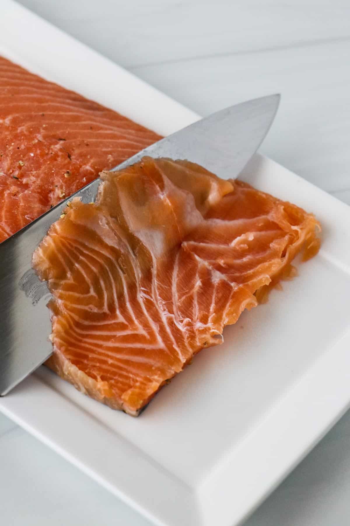 Person cutting through cured salmon with a knife.