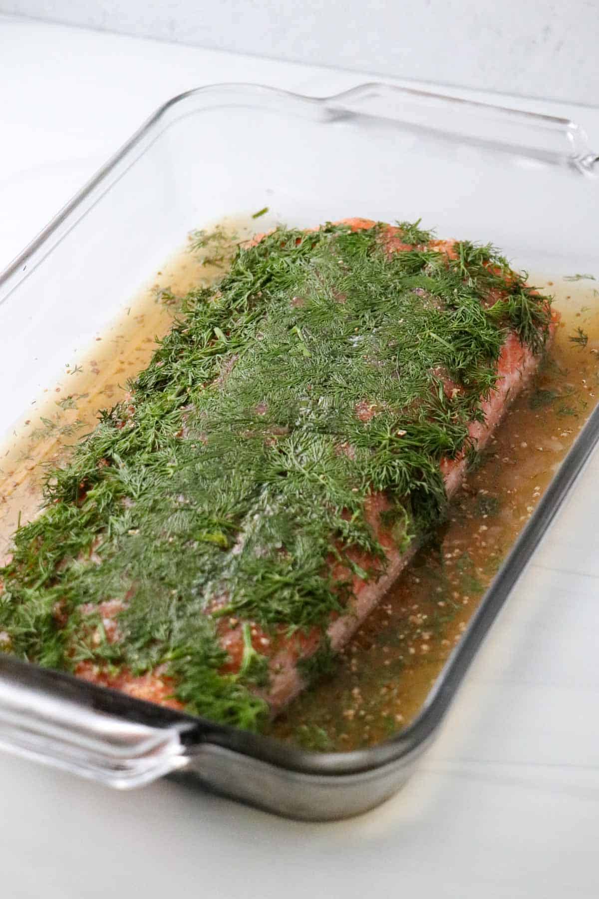 Cured salmon in a glass dish topped with chopped fresh dill.
