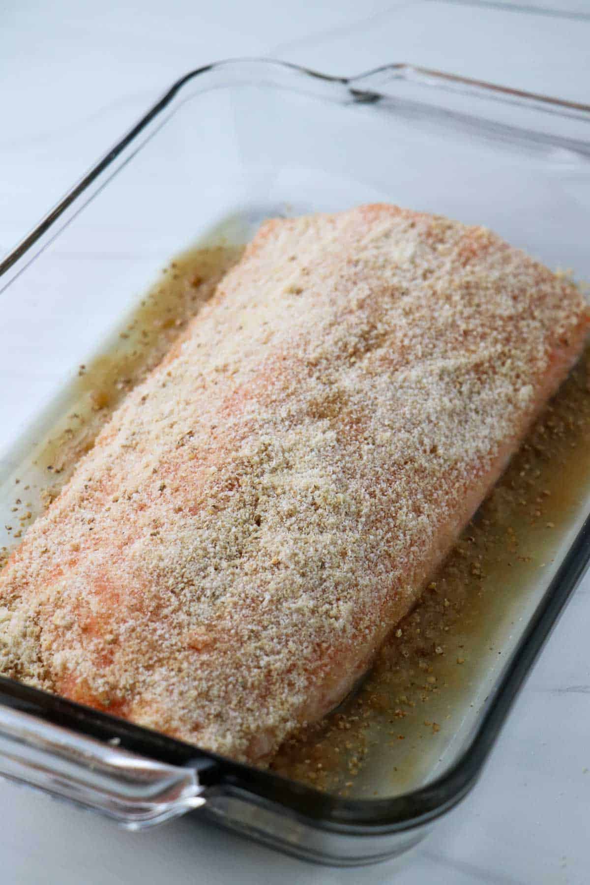 Salmon covered in salt and brown sugar in a glass dish.
