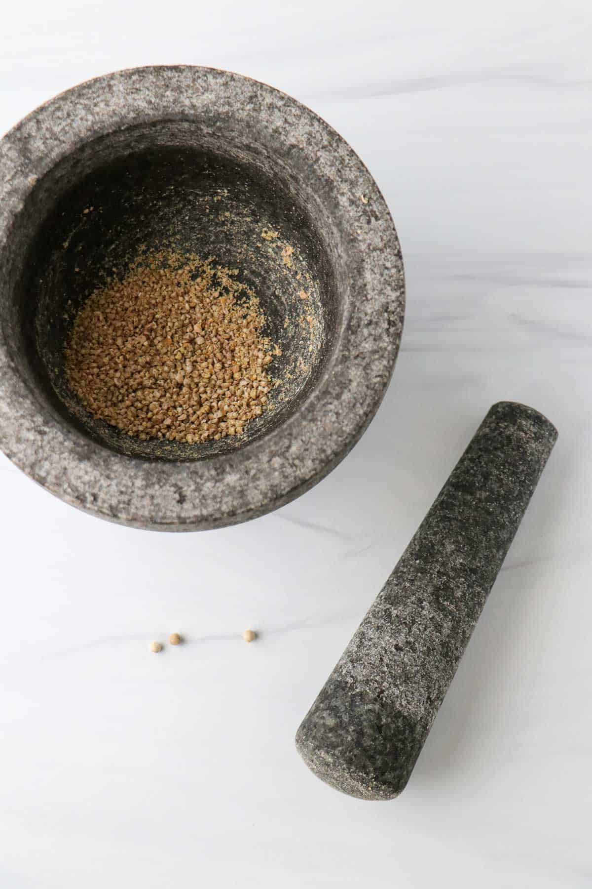 Ground white peppercorns in a mortar next to a pestle.