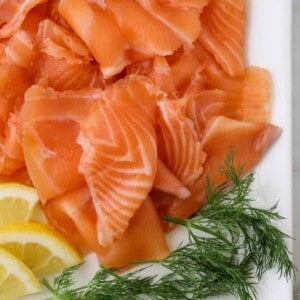 Close up of gravlax on a white platter with dill and lemons.