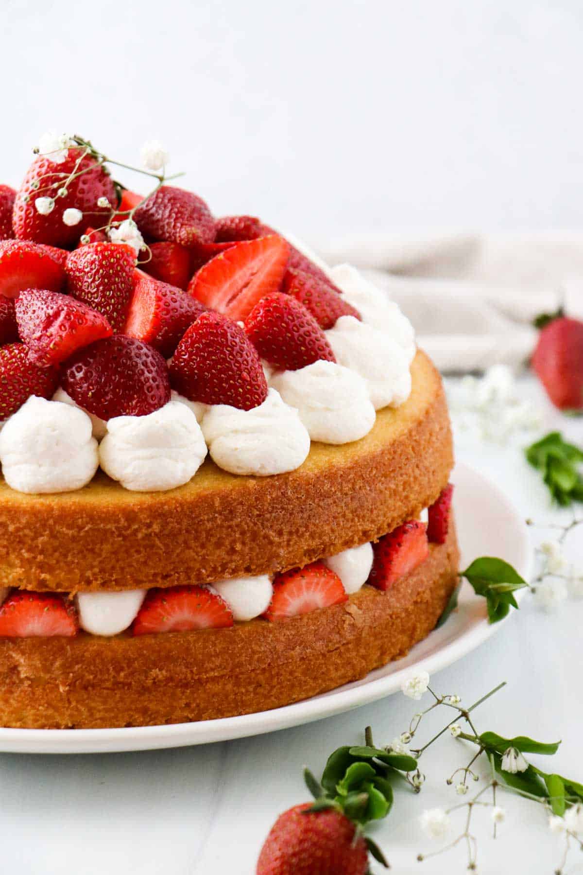 Layer cake topped with whipped cream and fresh strawberries next to flowers and strawberries.