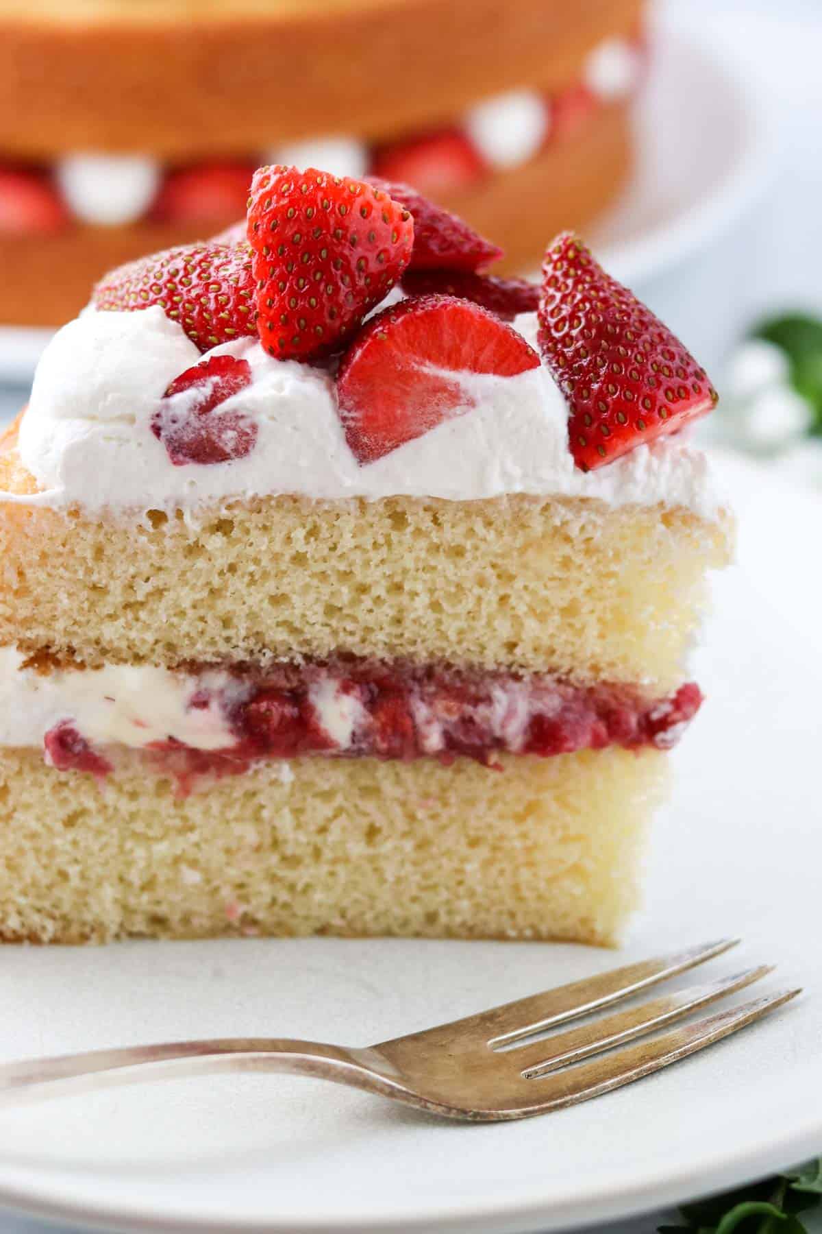 Upright slice of vanilla cake with strawberry filling next to a fork.