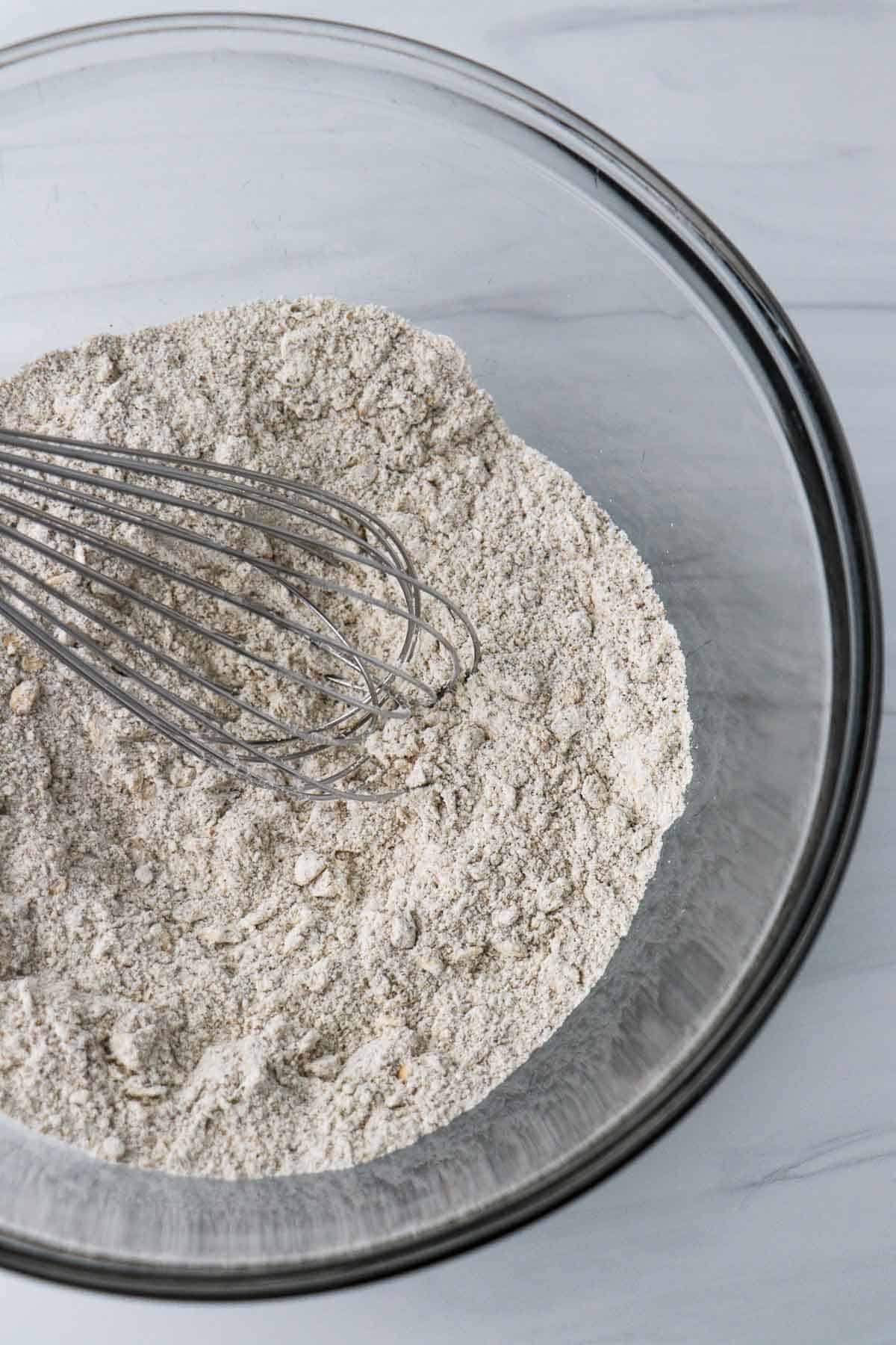 Flour and oats in a bowl with a whisk.