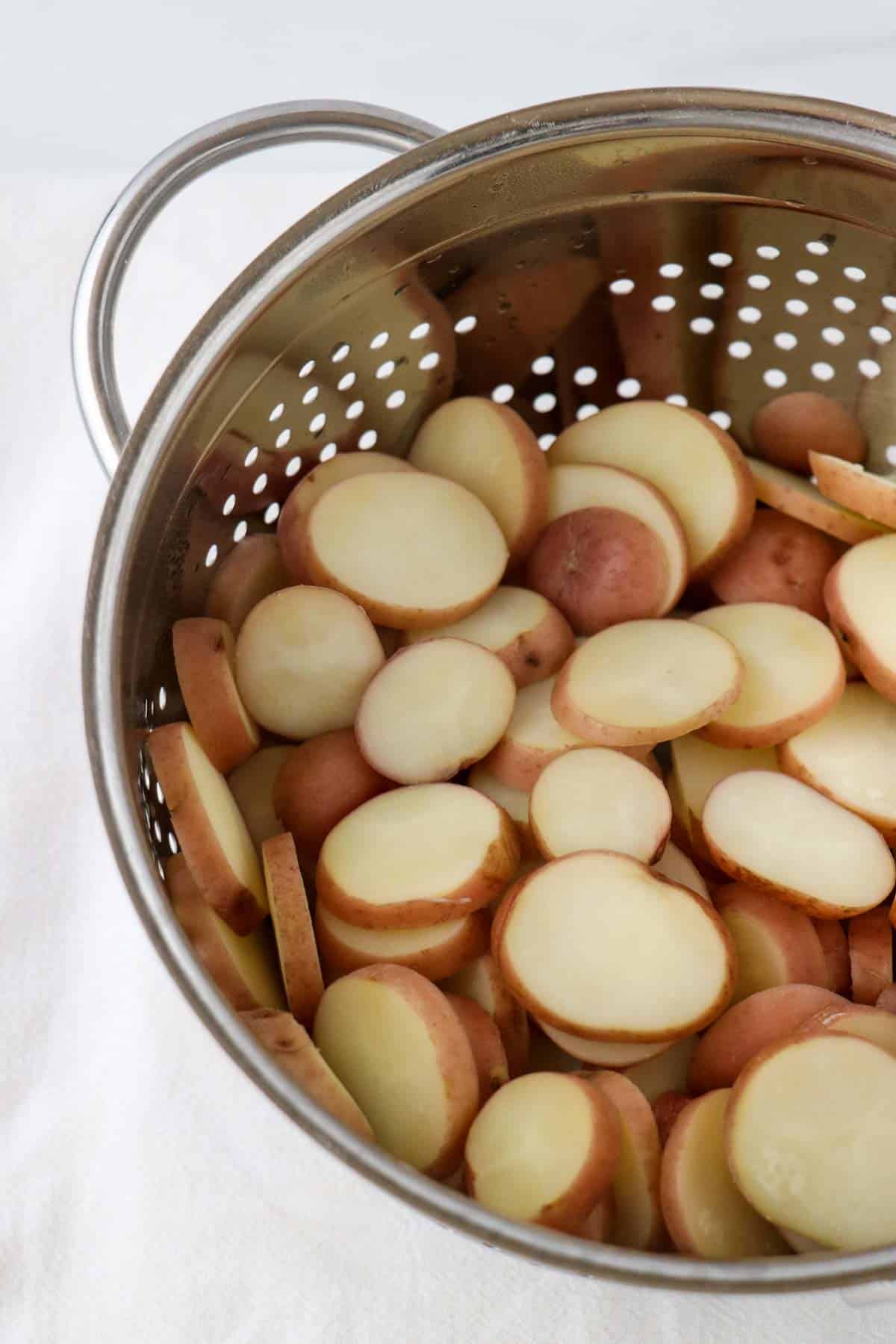 Sliced baby red potatoes in a metal colander.