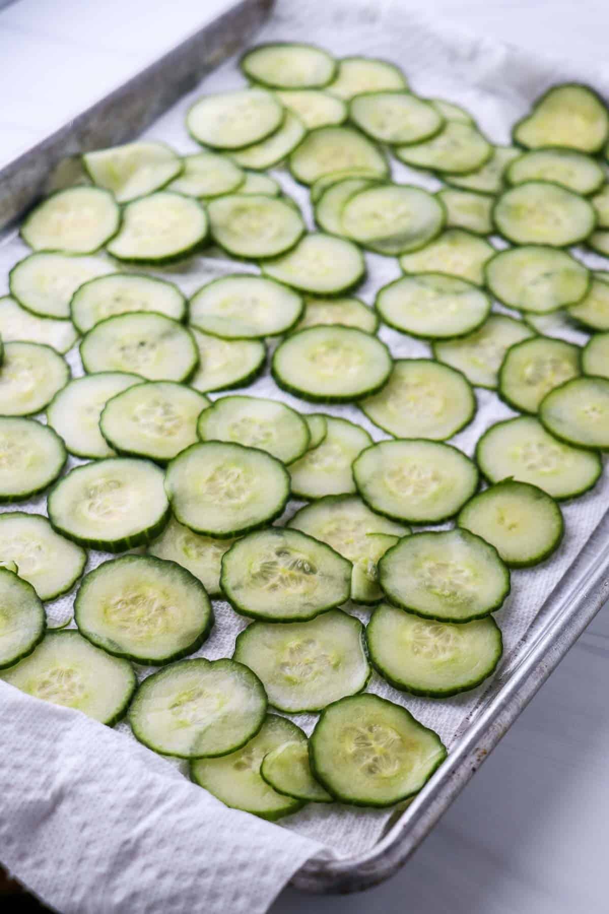 Slices of cucumber on paper towels in a rimmed baking sheet.