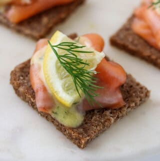 Close up of gravlax on rye bread topped with a lemon wedge and fresh dill.