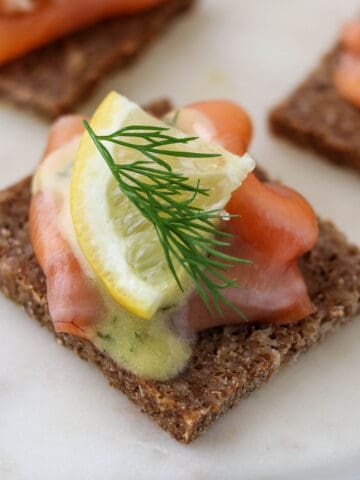 Close up of gravlax on rye bread topped with a lemon wedge and fresh dill.