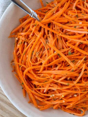 Raw carrot salad in a white bowl with a spoon.