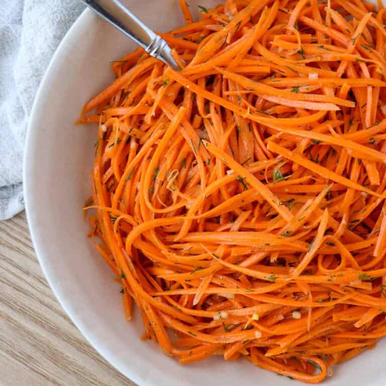 Raw carrot salad in a white bowl with a spoon.