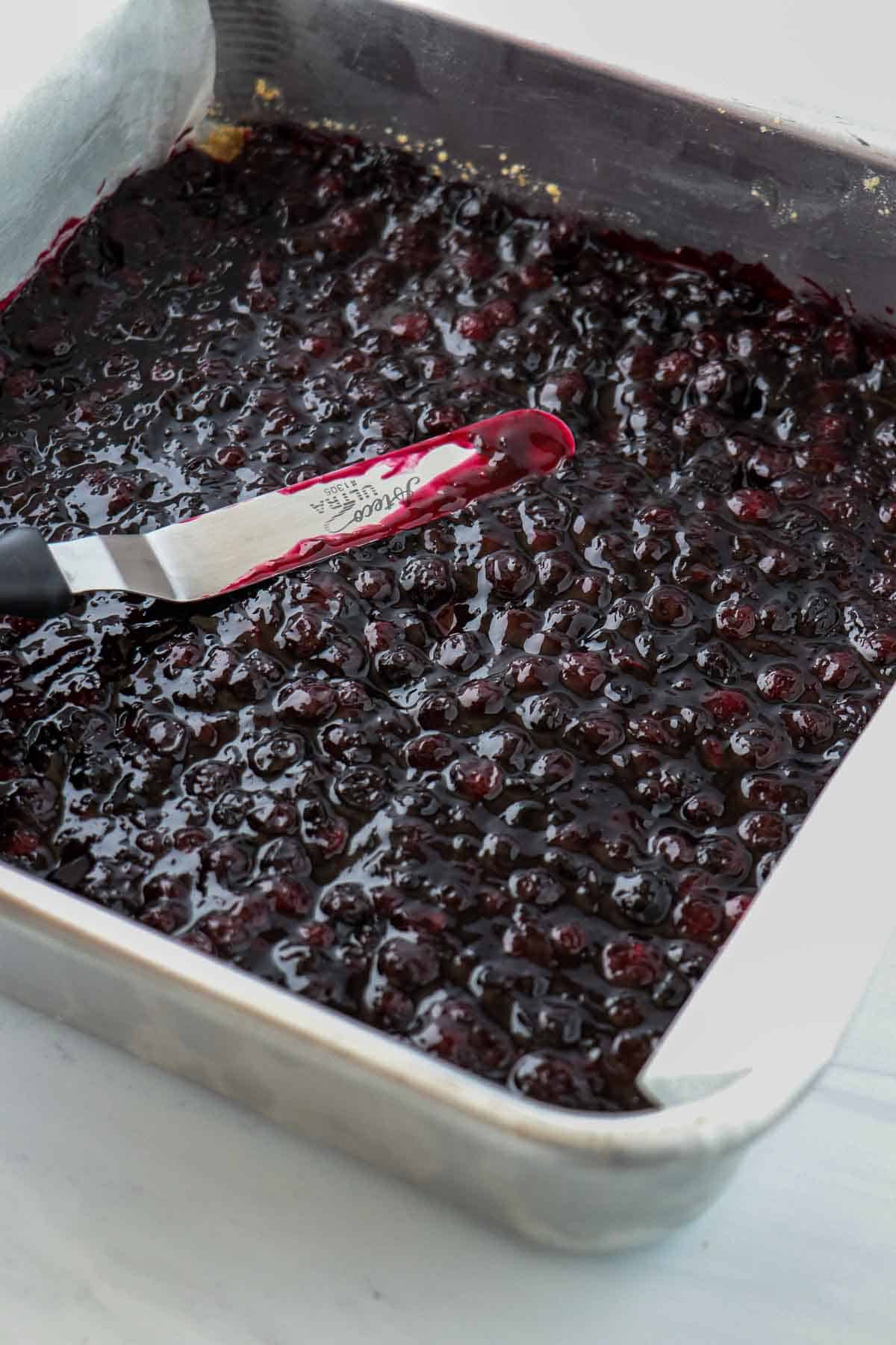Blueberry filling being spread in a square baking pan.