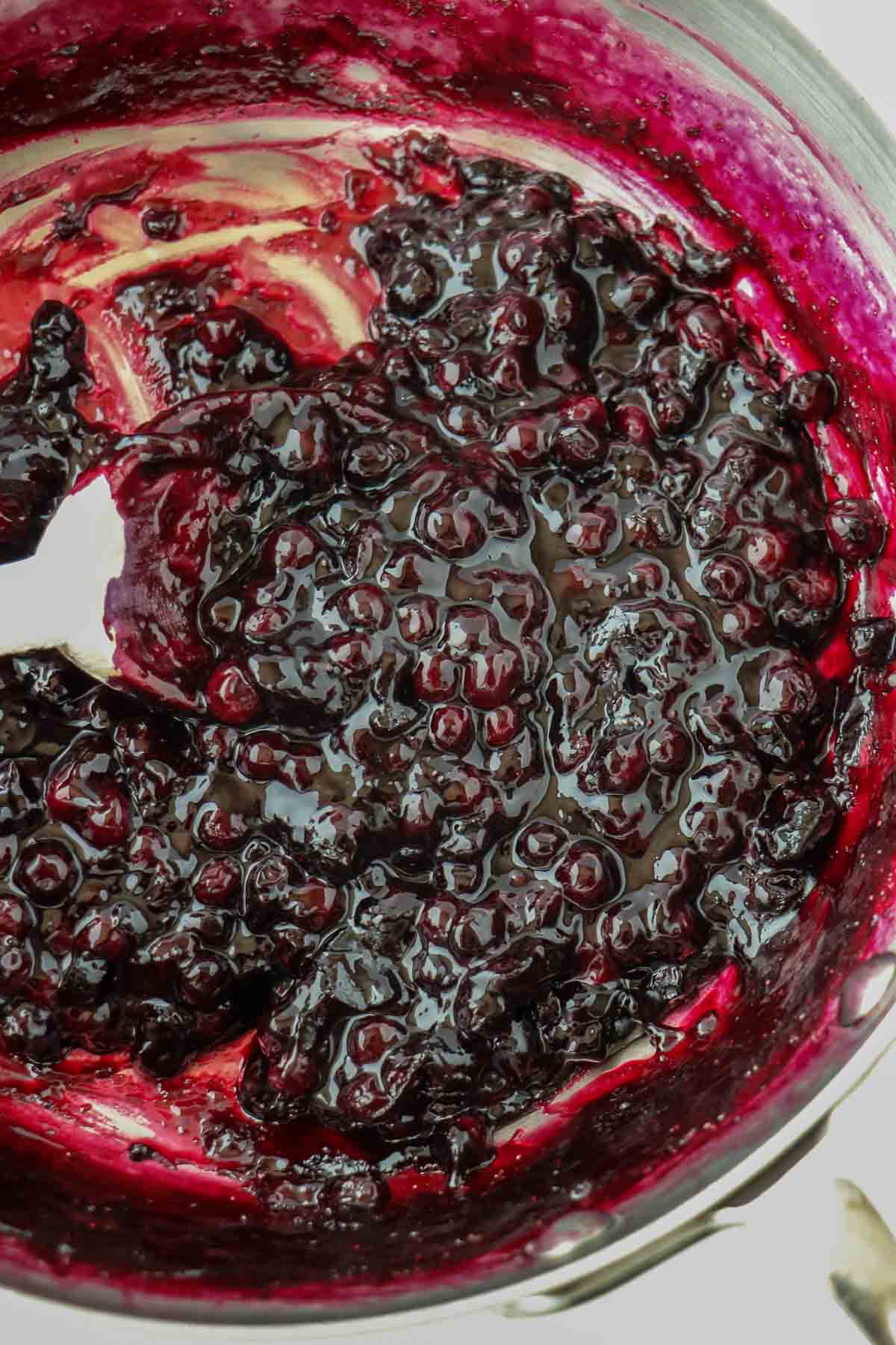 Blueberry filling in a pan with a wooden spoon.