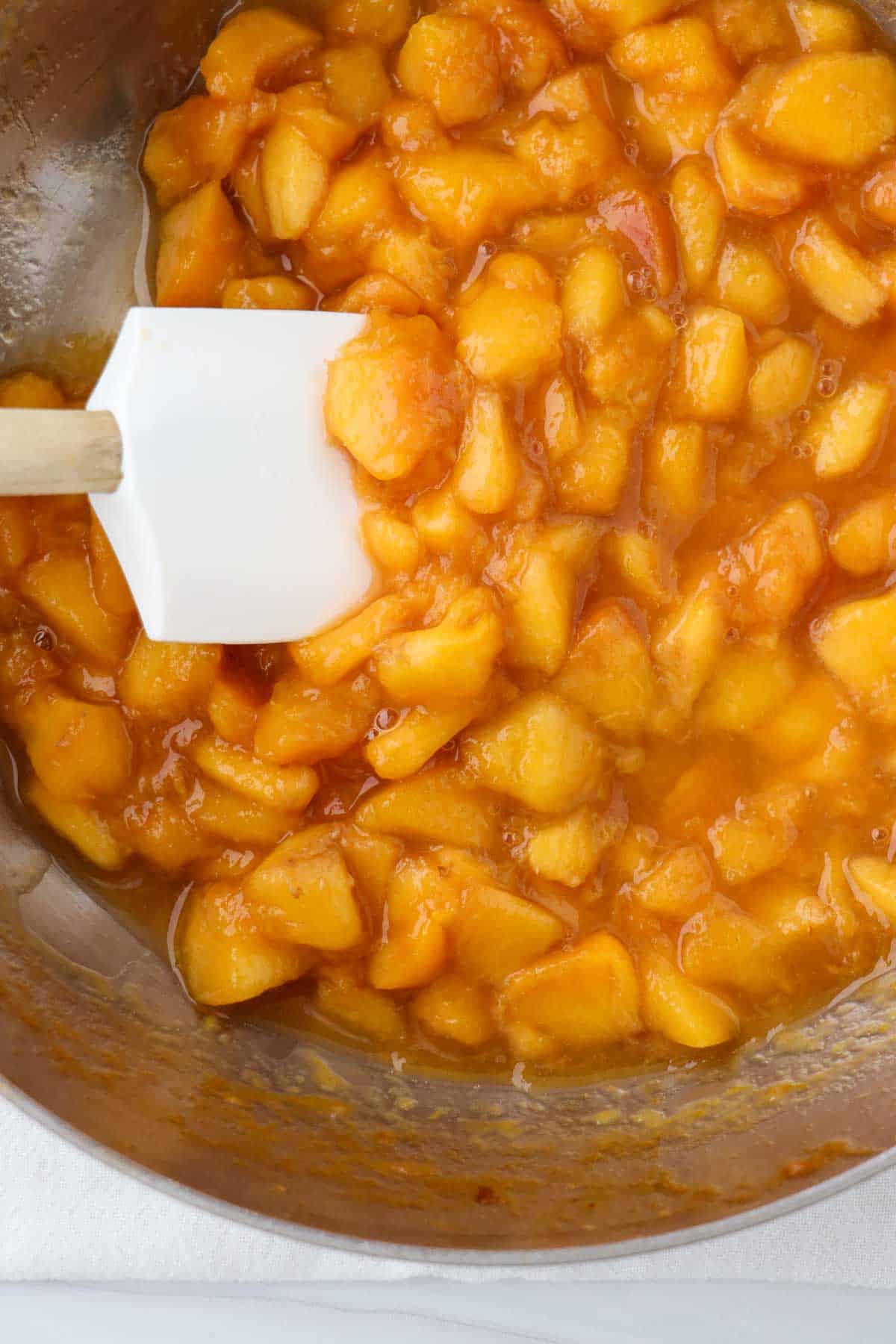 Peach compote in a saucepan with a rubber spatula.