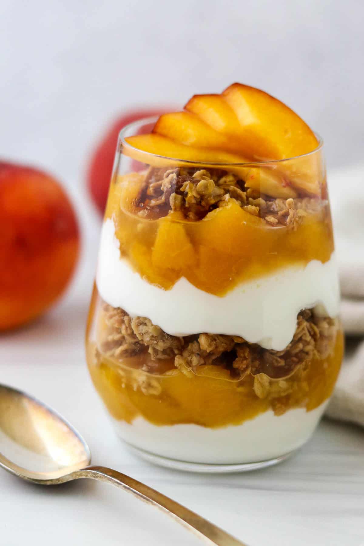 Yogurt and granola parfait layered with peach compote next to a spoon.