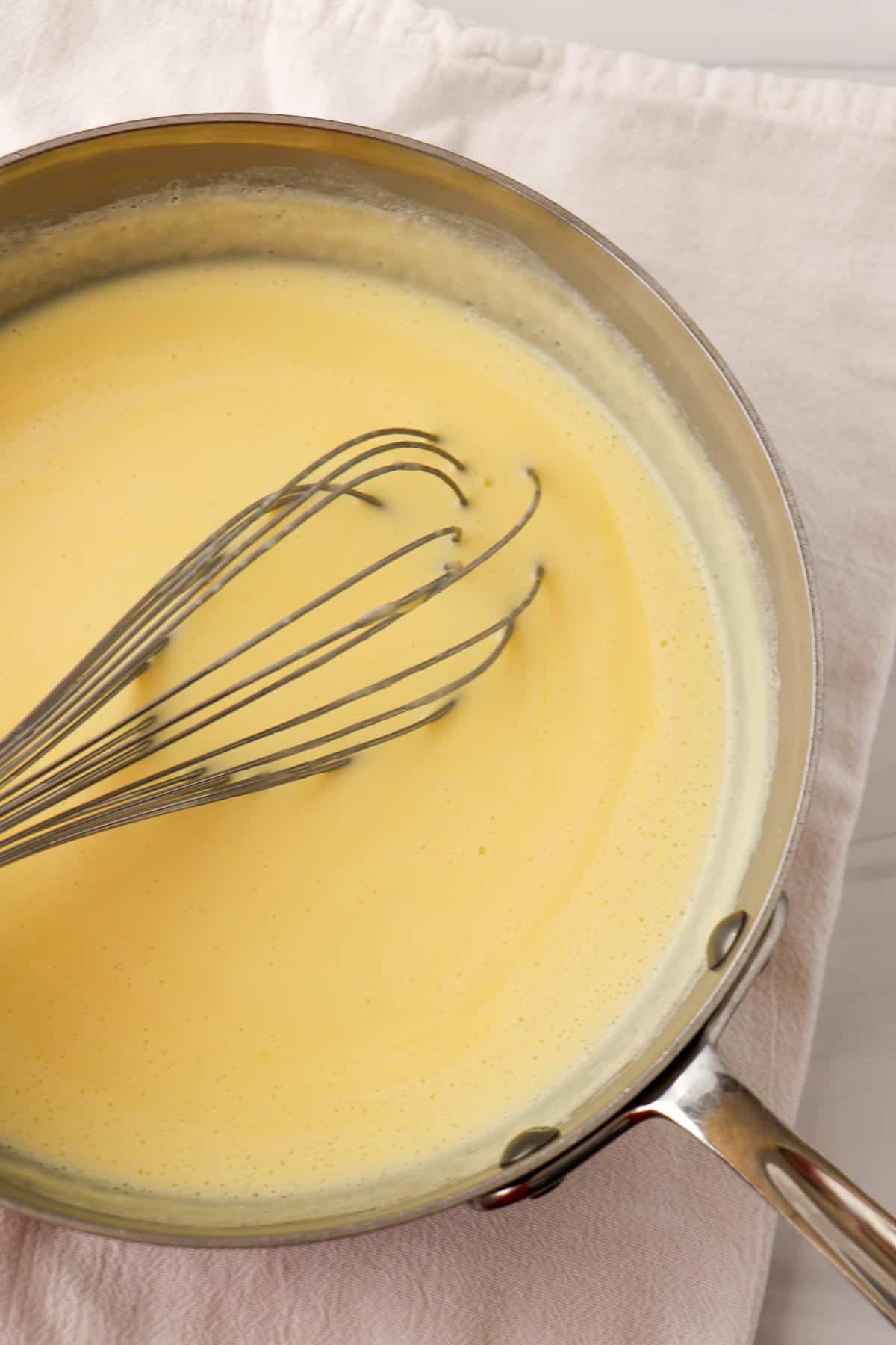 Ice cream custard in a saucepan with a whisk.