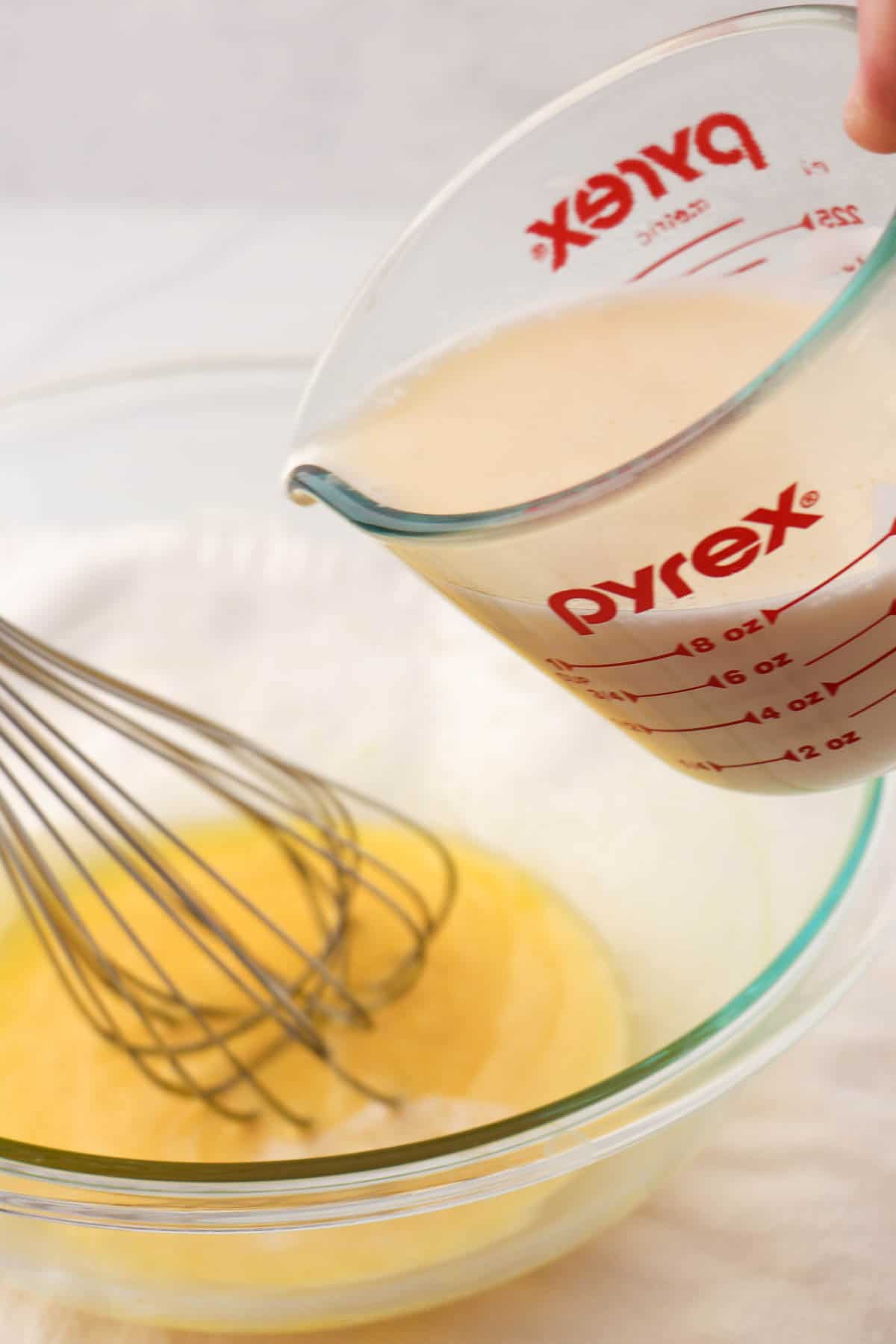 Person pouring cream into egg yolks in a bowl with a whisk.