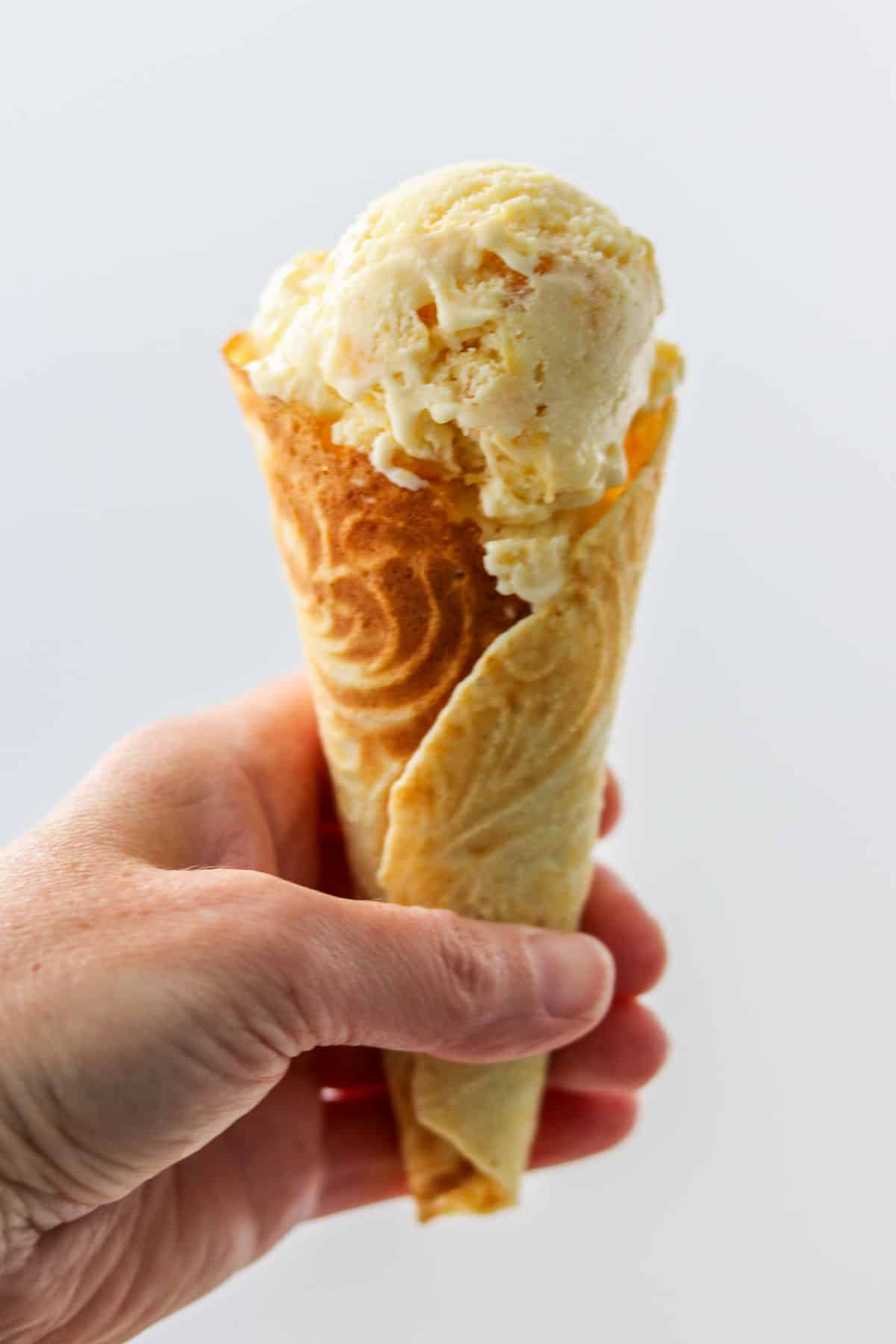 Person holding ice cream cone filled with peach ice cream.