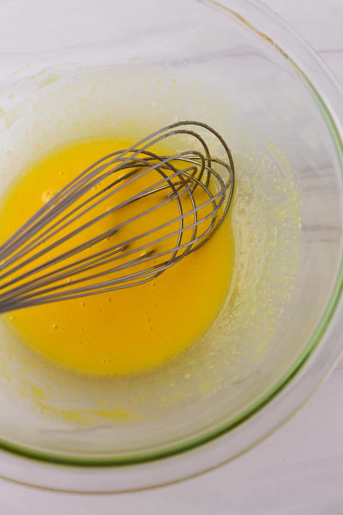 Egg yolks in a glass bowl with a whisk.
